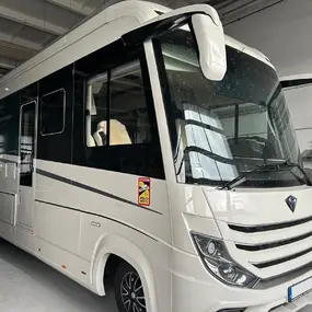 Modernes Wohnmobil mit großem Fahrerhaus und Panoramafenster in heller Werkstatthalle.